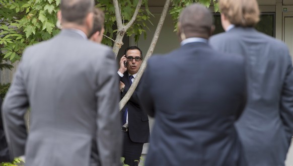 Security and staff members look on as U.S. Treasury Secretary Steven Mnuchin takes a phone call among the trees at a meeting for the G7 Finance and Central Bank Governors in Whistler, British Columbia ...