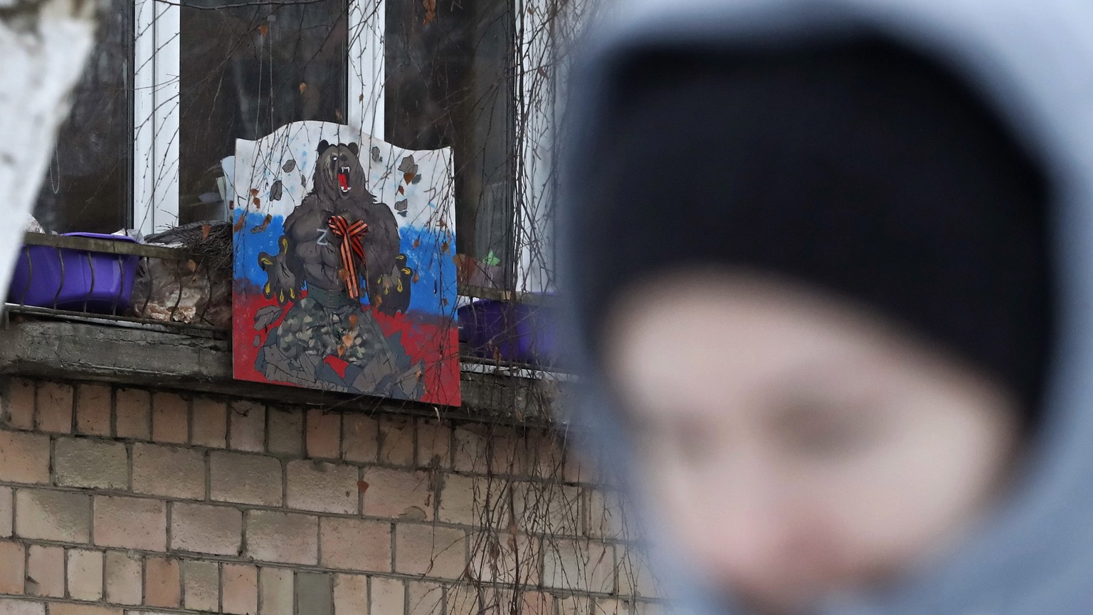 epa10439896 A woman walks next to a handmade poster with a letter Z in support of the Russian military, installed on a window of an apartment building in Moscow, Russia, January 30, 2023. The letters Z, V and ...