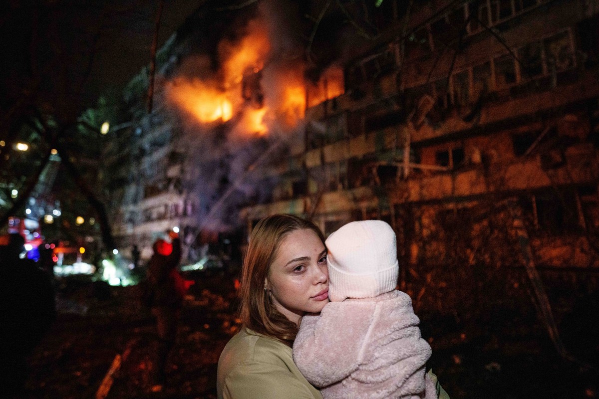 Victoria Deineko holds her daughter Mia while standing in front of a multi-story residential building damaged in a Russian missile strike in Kyiv, Ukraine, Tuesday, Oct. 13, 2026. (AP Photo/Evgeniy Ma ...
