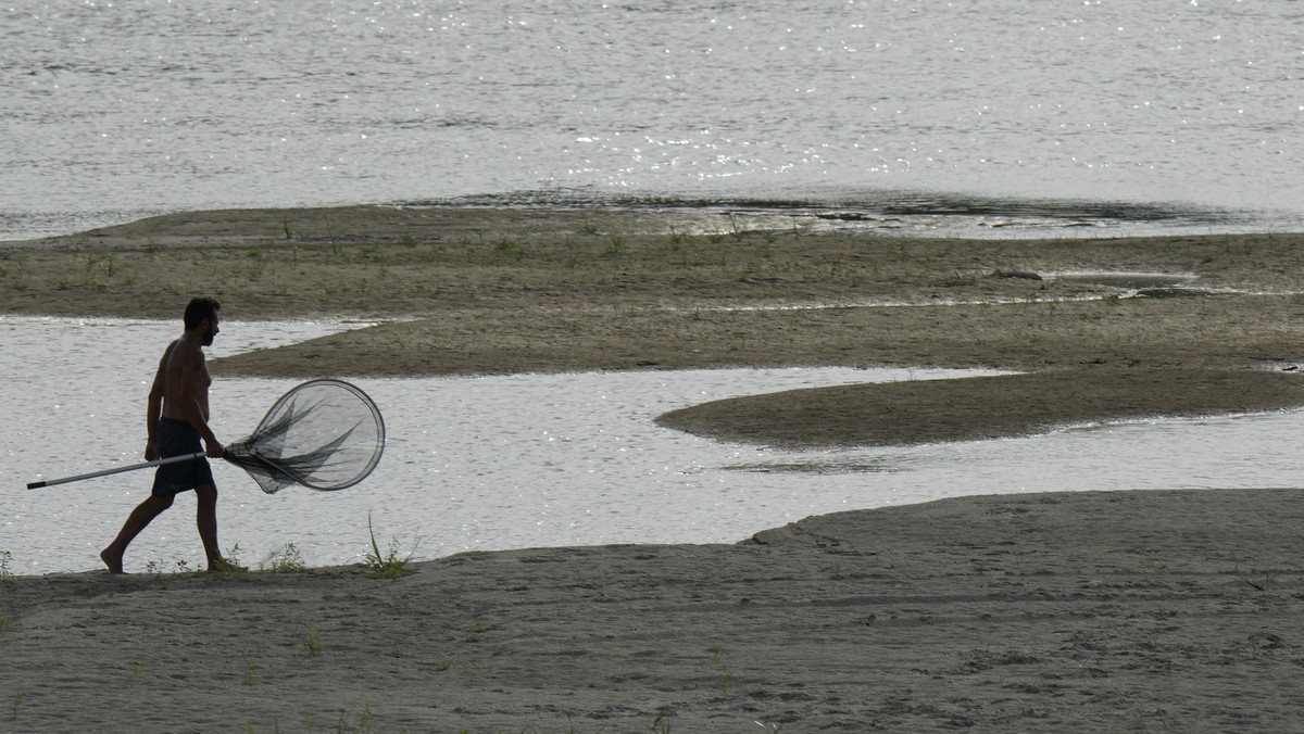 A fisherman walks on the dried riverbed at a tourist dock along the Po river in Ficarolo, Italy, Thursday, July 28, 2022. Italy's drought has dried up rivers crucial for irrigation threatening so ...