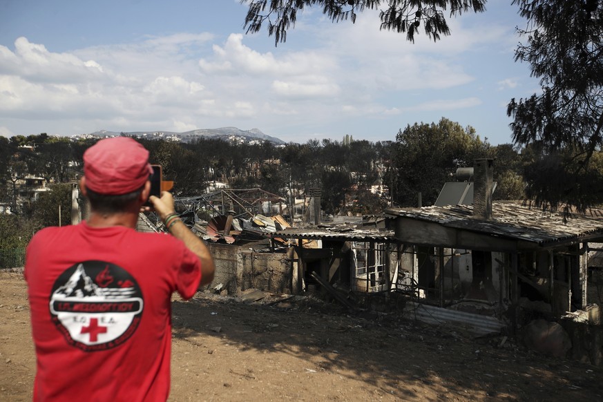 A member of a rescue team takes a photography the burned houses in Mati, east of Athens, Wednesday, July 25, 2018. Rescue crews were searching Wednesday through charred homes and cars for those still  ...