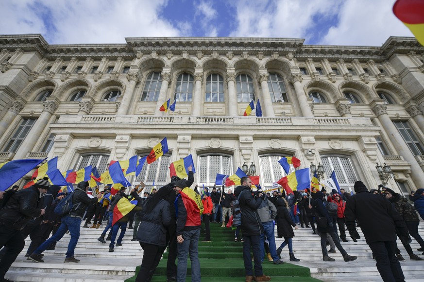 Anti-COVID-19 green pass protesters stand outside of the Palace of Parliament in Bucharest, Romania, Tuesday, Dec. 21, 2021. People gathered to protest against the introduction of the COVID-19 &quot;g ...