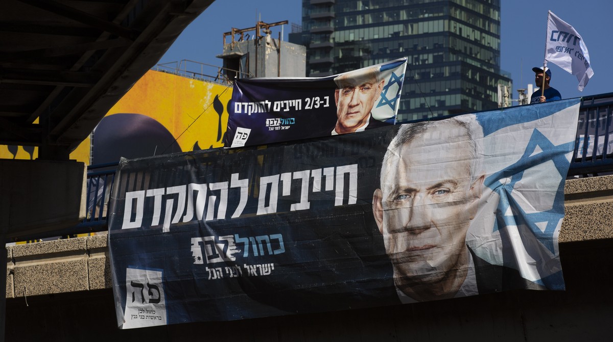 Blue and White party activist waves a flag behind an election campaign billboard that shows the party's leader Benny Gantz, in Tel Aviv, Israel, Sunday, March. 1, 2020. Israel heads into its thir ...