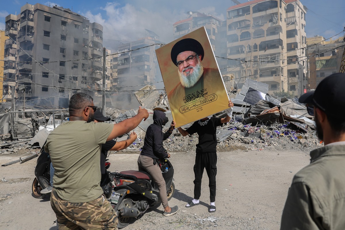 epa11637955 A Hezbollah supporter holds a placard with Hezbollah leader Hassan Nasrallah next to the rubble of a completely destroyed building in Dahieh, a southern suburb controlled by Hezbollah, Bei ...