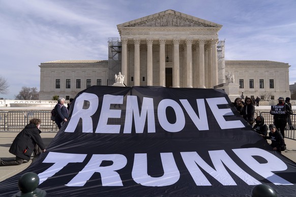 Demonstrators hold a banner outside of the U.S. Supreme Court, Thursday, Feb. 8, 2024, in Washington. The U.S. Supreme Court on Thursday will take up a historic case that could decide whether Donald T ...
