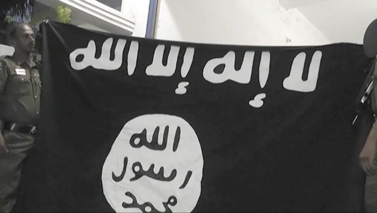 In this Friday, April 26, 2019, image made from video, officers hold up an Islamic State group flag in Arabic that reads: "There is no God, but Allah" and "Allah, Prophet, Muhammad&quot ...