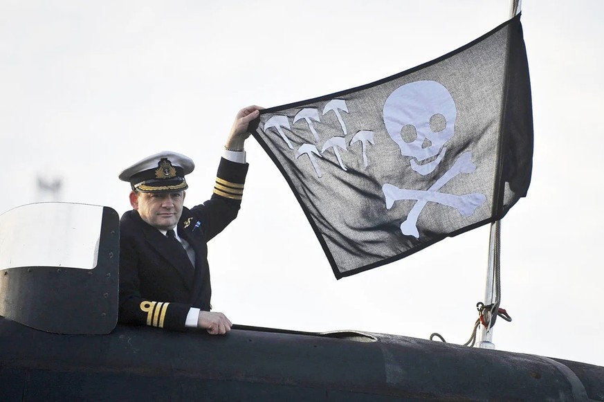 Britain’s Royal Navy Commander Rob Dunn holds a Jolly Roger flag on HMS Triumph as she sails back into Davenport, Plymouth, Devon, England, Saturday, April 2, 2011 after taking part in operations in t ...