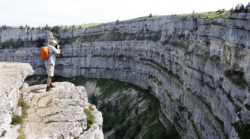 Ein Ausfluegler geniesst die Aussicht zum Creux du Van, am Samstag, 19. Juli 2014, bei Noiraigue. Der Creux du Van im Schweizer Jura an der Grenze zwischen den Kantonen Neuenburg und Waadt ist etwa 12 ...