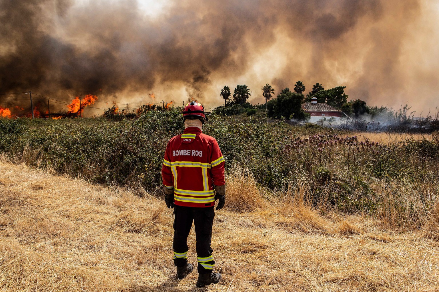 epa10069330 A firefighter watches the flames near a house threatened by a fire in the Ludo area, Faro, Algarve, south of Portugal, 13 July 2022. Sixteen of the 18 districts of mainland Portugal are un ...