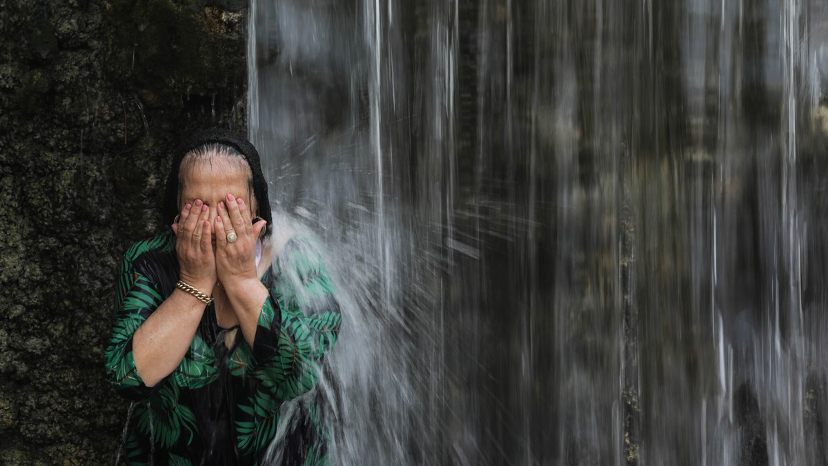 epa10798662 A woman cools off in a waterfall on extreme hot summer day in Sakhne Park, also known as Gan HaShlosha National Park, near Beit Shean, northern Israel, 13 August 2023. According to the met ...