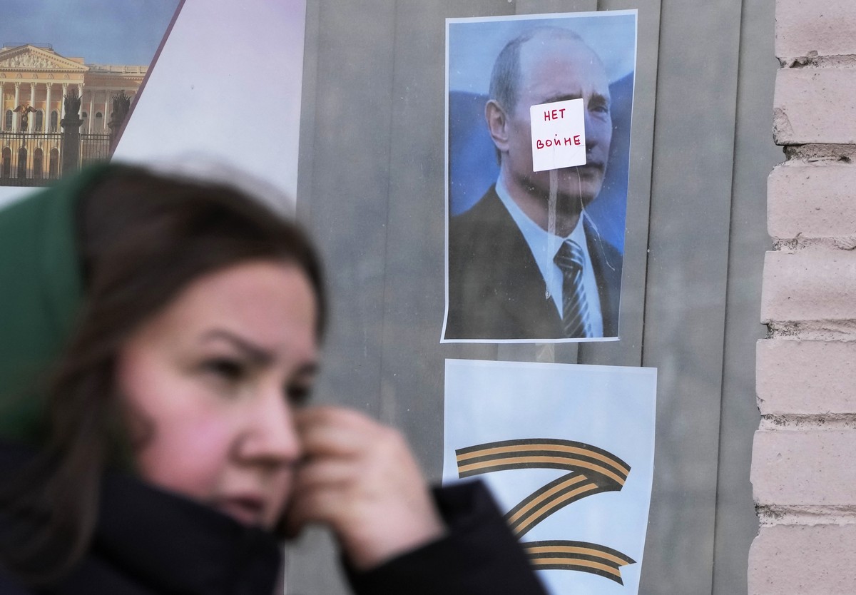 A woman walks past a 'No War' sign stuck on a portrait of Russian President Vladimir Putin, on the window of a children's library in St. Petersburg, Russia, Tuesday, March 29, 2022. (AP ...