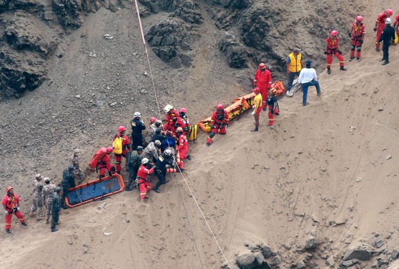 In this photo provided by the government news agency Andina, rescue workers surround an injured man on a stretcher who was lifted up from the site of a bus crash at the bottom of a cliff, after the bu ...