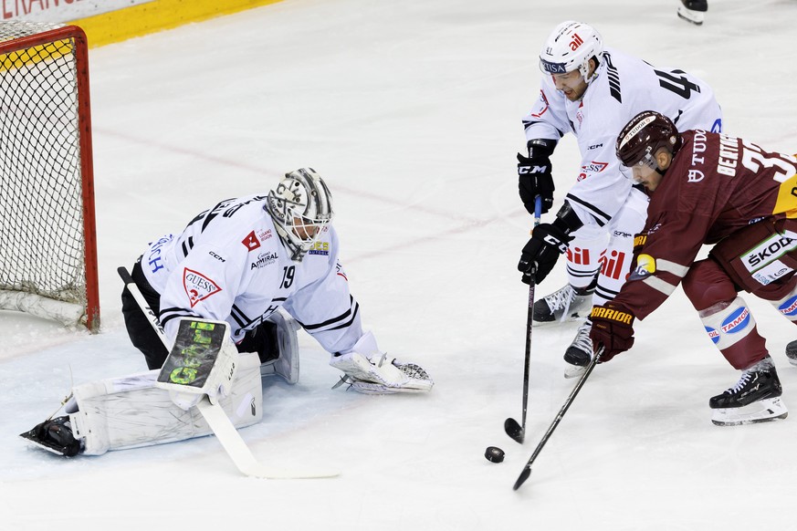 Lugano&#039;s defender Lukas Klok, centre, vies for the puck with Geneve-Servette&#039;s forward Alessio Bertaggia, right, past Lugano&#039;s goaltender Mikko Koskinen, left, during a National League  ...