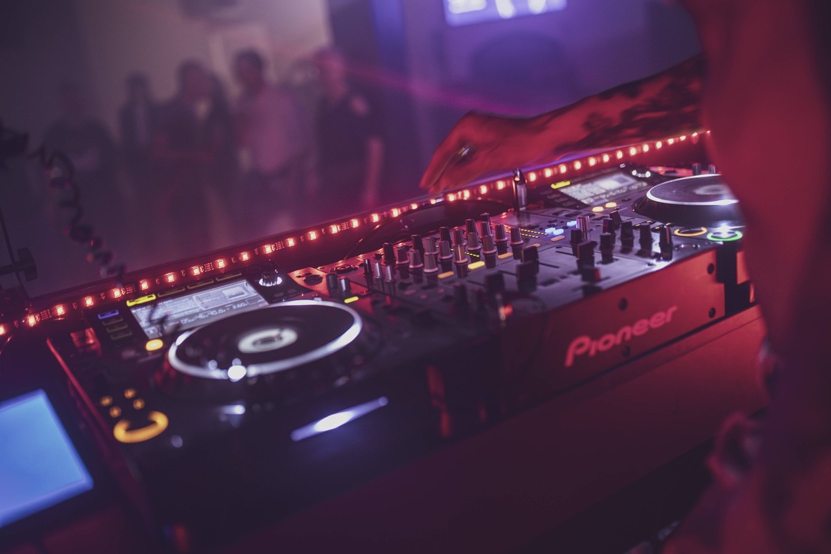 Rome, italy 4 may 2025: dj mixing music on a pioneer console at a nightclub with red and purple lights and blurred people dancing in the background Dj playing music at a nightclub party using pioneer  ...