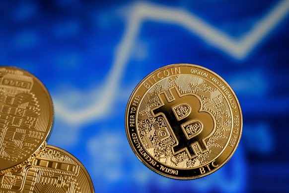 epa09018336 A bitcoin reflects in front of a monitor showing a stock barometer in Duesseldorf, Germany, 17 February 2021. For the first time, the cryptocurrency Bitcoin has exceeded the mark of 50,000 ...