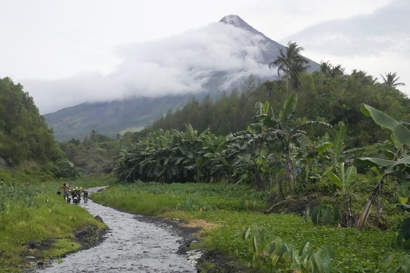 Men wash their motorcycles along a stream near Mayon volcano in Bonga, Albay province, northeastern Philippines, Saturday, June 10, 2023. Monsoon rains that could be unleashed by an offshore typhoon w ...