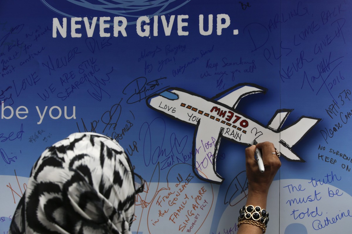 epa05197357 A woman writes messages for the passengers of missing Malaysia Airlines flight MH370 on a banner during a remembrance ceremony to mark the second anniversary of the plane's disappeara ...