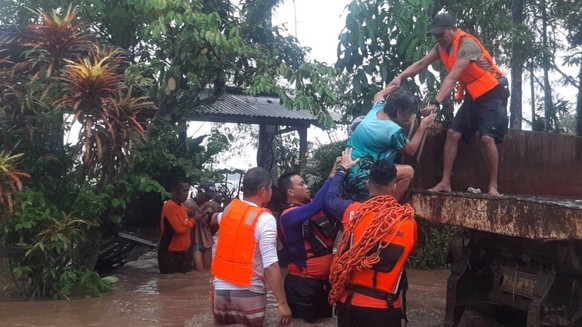 epa10379154 A handout photo made available by the Philippine Coast Guard (PCG) shows coast guard personnel assisting a resident during a rescue operation in the flood-hit town of Plaridel, Misamis Occ ...