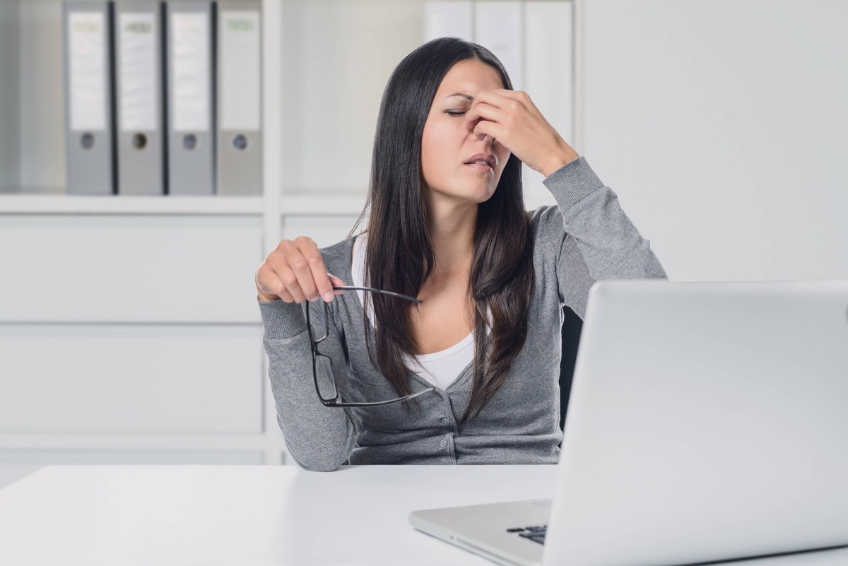 CVS: Junge Frau, die unter einer Überanstrengung der Augen an ihrem Laptop leidet, nimmt ihre Brille ab und reibt sich mit schmerzverzerrtem Gesichtsausdruck die Augen.