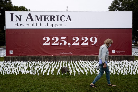 epa08777748 A man walks in front of a sign showing a number representing a recent official US COVID-19 death toll, at a memorial for people who died with COVID-19, at the DC Armory Parade Ground outsi ...