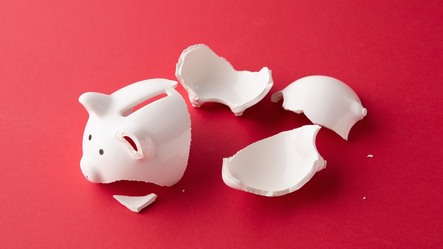 Broken whiter ceramic piggy bank in pieces on red surface