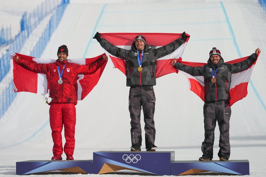 From left, silver medalist Canada's Eliot Grondin, gold medalist Austria's Alessandro Haemmerle and bronze medalist Austria's Jakob Dusek celebrate with flags during the men's snow ...
