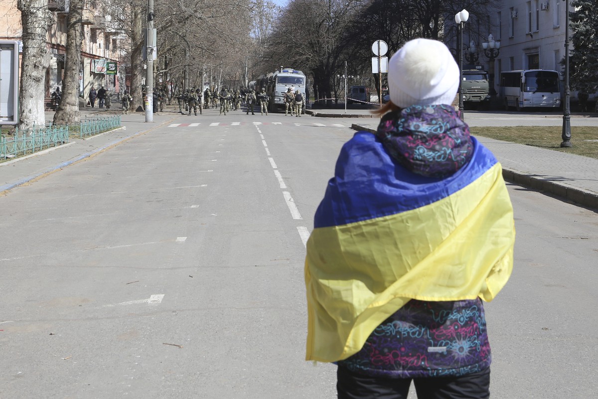 FILE - A woman covered by Ukrainian flag stands in front of Russian troops in a street during a rally against Russian occupation in Kherson, Ukraine, Saturday, March 19, 2022. The southern city of Khe ...