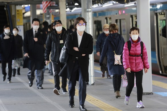 People wearing face masks to protect against the spread of the coronavirus walk at a platform at a train station in Tokyo, Monday, Feb. 1, 2021. (AP Photo/Koji Sasahara)