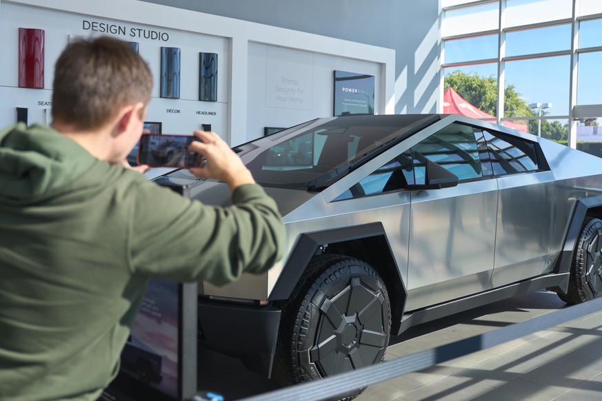 epa11006473 A man takes a picture of a Tesla Cybertruck on display at Tesla in Buena Park, California, USA, 01 December 2023. After four years of delays and complications, the Tesla Cybertruck was rel ...