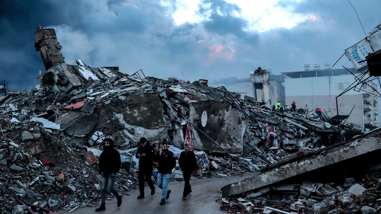 epa10452169 People walk at the site of a collapsed building following an earthquake in Iskenderun, district of Hatay, Turkey, 07 February 2023. More than 4,000 people were killed and thousands more in ...