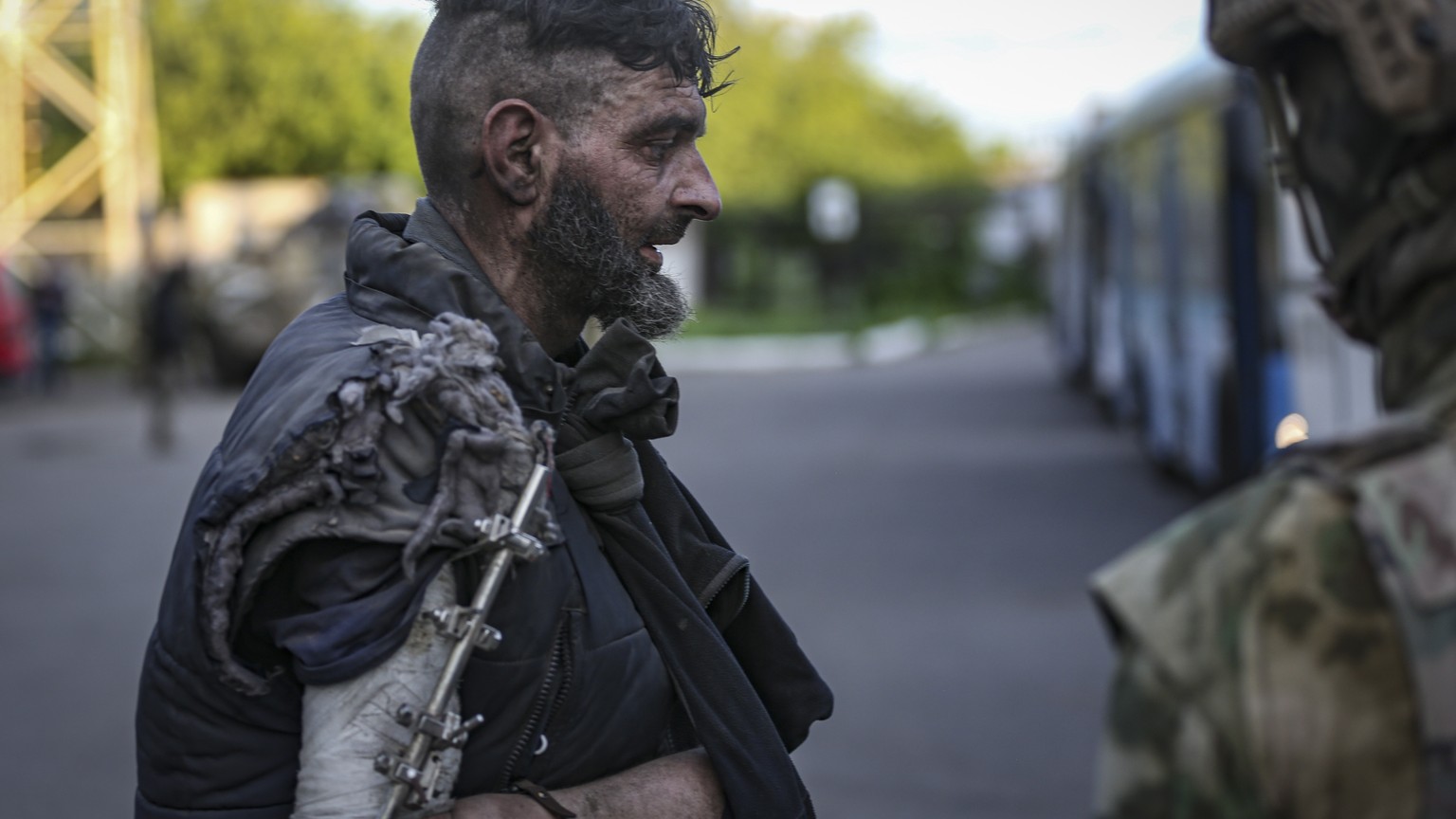 epa09953883 Self-proclaimed DPR militia (R) watches an Ukrainian serviceman boarding a bus as he is being evacuated from the besieged Azovstal steel plant in Mariupol, Ukraine, 17 May 2022. A total of ...