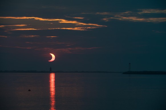 A partial solar eclipse is seen as the sun rises behind the Delaware Breakwater Lighthouse, Thursday, June 10, 2021, at Lewes Beach in Delaware. The annular or “ring of fire” solar eclipse is only vis ...