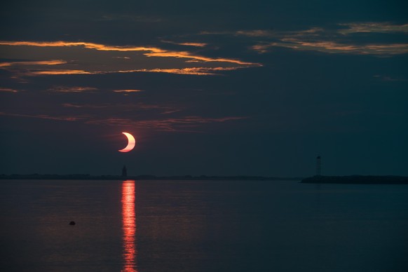 A partial solar eclipse is seen as the sun rises behind the Delaware Breakwater Lighthouse, Thursday, June 10, 2021, at Lewes Beach in Delaware. The annular or “ring of fire” solar eclipse is only vis ...