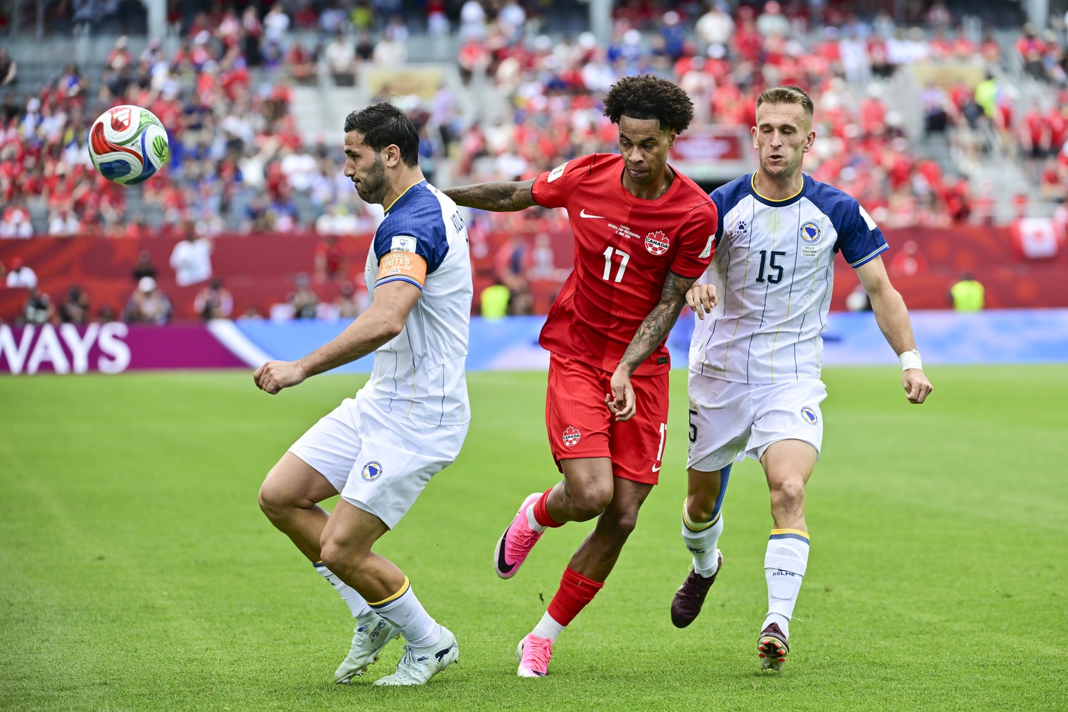epa13033634 Sead Kolasinac (L) and Amar Memic (R) of Bosnia and Herzegovina in action against Tajon Buchanan (C) of Canada during the FIFA World Cup 2026 group stage match Canada against Bosnia and He ...