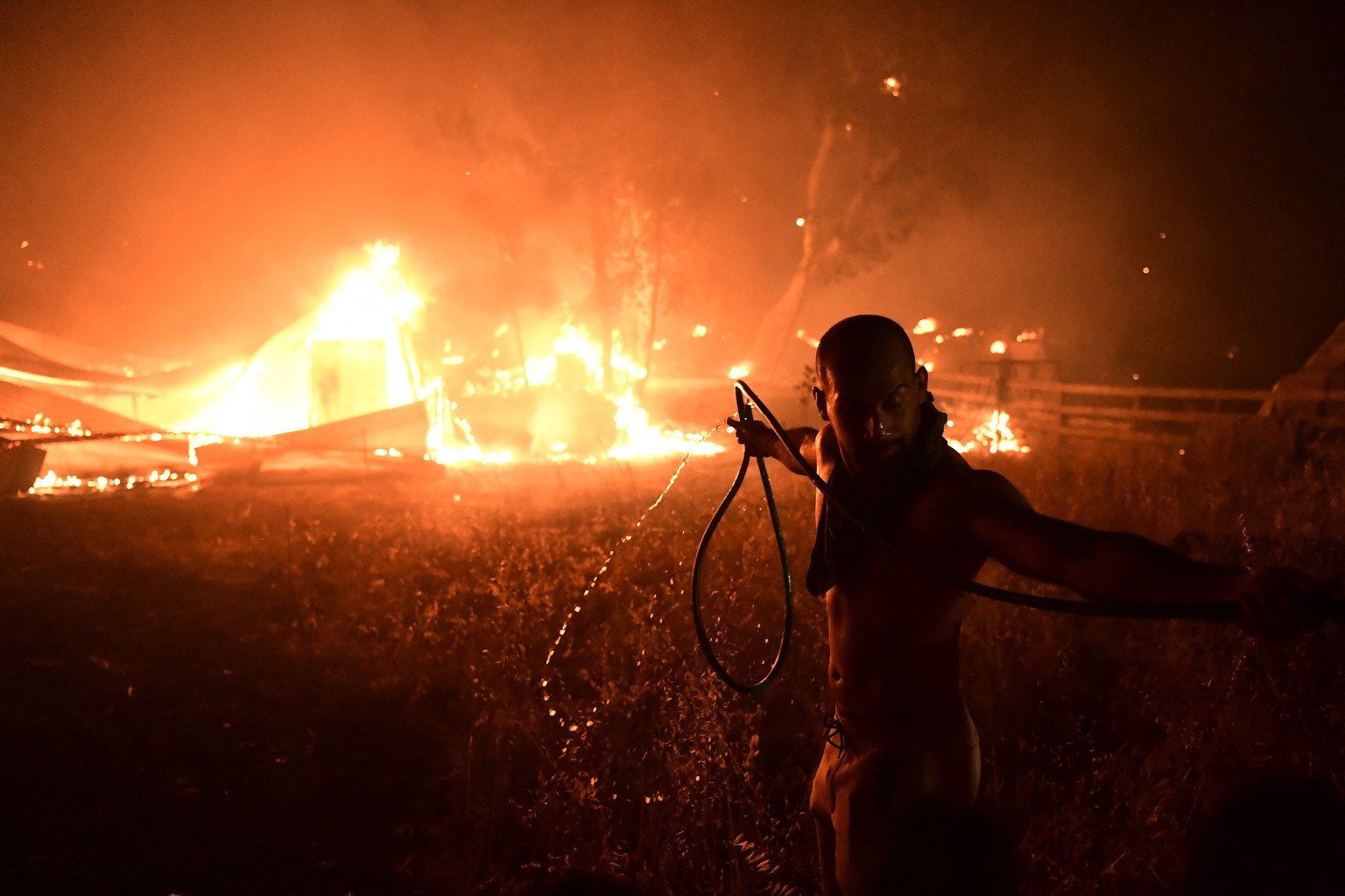 A man uses a water hose during a wildfire in Adames area, in northern Athens, Greece, Tuesday, Aug. 3, 2021. Thousands of people fled their homes north of Athens on Tuesday as a wildfire broke out of  ...