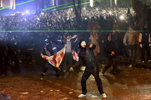 A masked demonstrator throws an object toward police during a rally against the governments&#039; decision to suspend negotiations on joining the European Union for four years, outside the parliament& ...