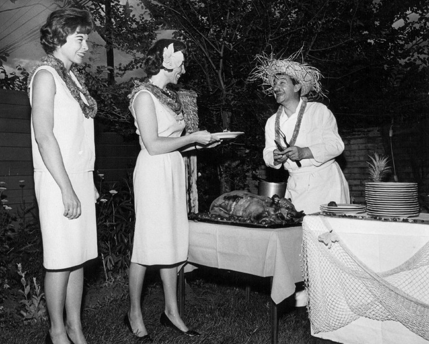 JUN 26 1964, JUL 1 1964 Luau Guests Sample Roast International House Chef Maurice Thuillier of 1450 Forest St., prepares to slice a roast pig for Miss Judine Siems (left) of Lincoln, Neb., and Miss Ma ...