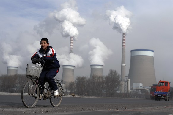 FILE - In this Dec. 3, 2009 file photo, a Chinese boy cycles past cooling towers of a coal-fired power plant in Dadong, Shanxi province, China. Led by cutbacks in China and India, construction of new  ...