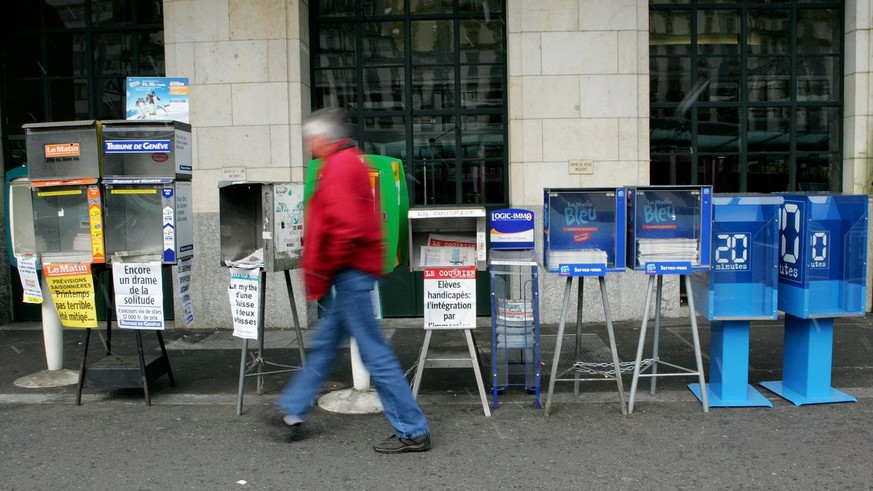 Une personne passe devant des caissettes de journaux ou deux caissettes du nouveau quotidien gratuit &quot;20 minutes&quot; ont ete posees devant la gare CFF de Cornavin, ce mardi 7 mars 2006 a Geneve ...