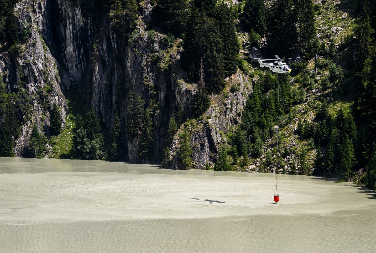 epa10753307 A Super Puma helicopter refills its bucket with water over Gibidum dam to extinguish forest fire above the communes of Bitsch and Ried-Moerel, in Naters, Switzerland, 18 July 2023. A fores ...