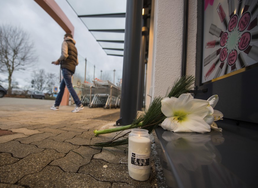 In this Dec. 27, 2017 photo. a customer leaves a drugstore in Kandel, Germany. Flowers and candles lie in front of the entrance. A 15-year-old Afghan asylum-seeker is in custody in Germany after alleg ...