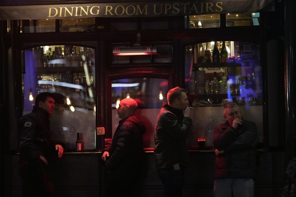 Customers stand outside pub in London, Friday, Dec. 17, 2021. On what would normally be one of the busiest times for pubs and restaurants just before Christmas, customer numbers are down in central Lo ...