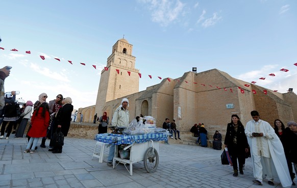 People pass a street vendor selling traditional confectioneries in front of the Uqba ibn Nafi mosque, also known as the Great Mosque, during a celebration to mark the birthday anniversary of Prophet M ...