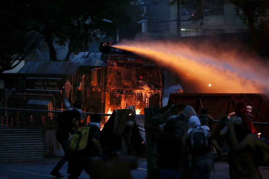 Ein vergitterter Wasserwerfer der Polizei versucht, in der Nacht auf den 20. April 2014 in Caracas, brennende Barrikaden zu löschen.&nbsp;