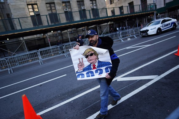 epa10558071 A Trump supporter walks with a sign past the media gathered across the street from the New York Criminal Court in New York, New York, U.S., April 04, 2023. A Manhattan grand jury voted to indict against former...