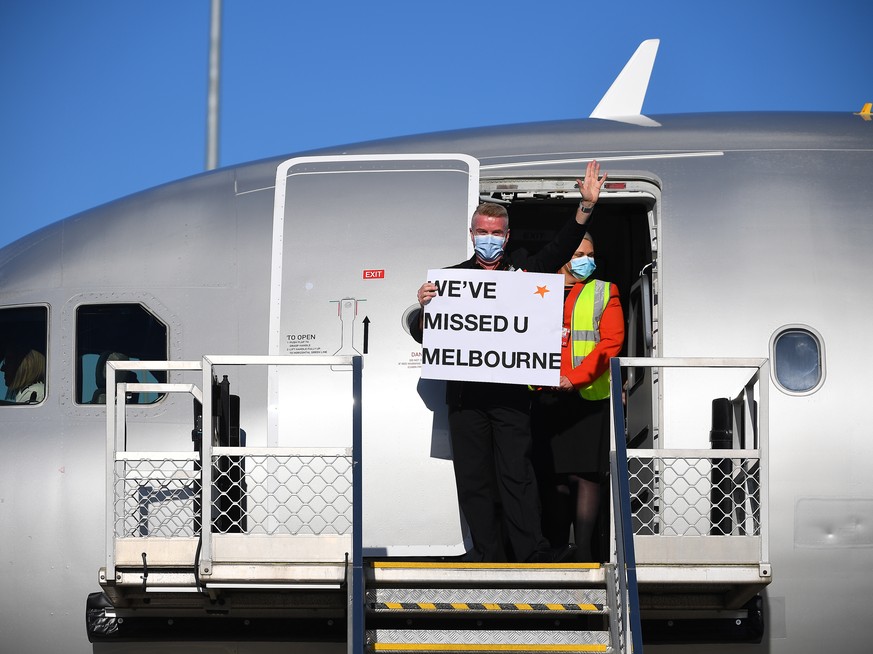 epa09556839 Flight crew wave to media holding a sign in the doorwell of Jetstar flight JQ505 which arrived from Sydney at Tullamarine Airport in Melbourne, Australia, 01 November 2021. The first passe ...