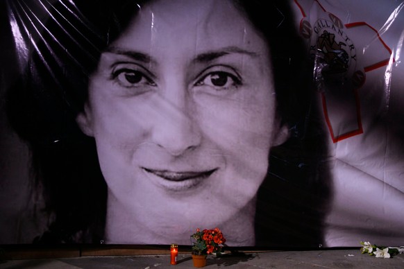 FILE - Flowers and a candle lie in front of a portrait of slain investigative journalist Daphne Caruana Galizia during a vigil outside the law courts in Valletta, Malta, Oct. 16, 2018. (AP Photo/Jonat ...