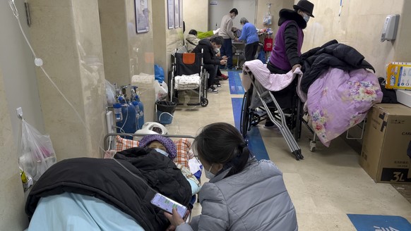 People tend to their elderly relatives rest along a corridor to provide intravenous drips at the emergency ward of a hospital in Beijing, Tuesday, Jan. 3, 2023. As the virus continues to rip through C ...