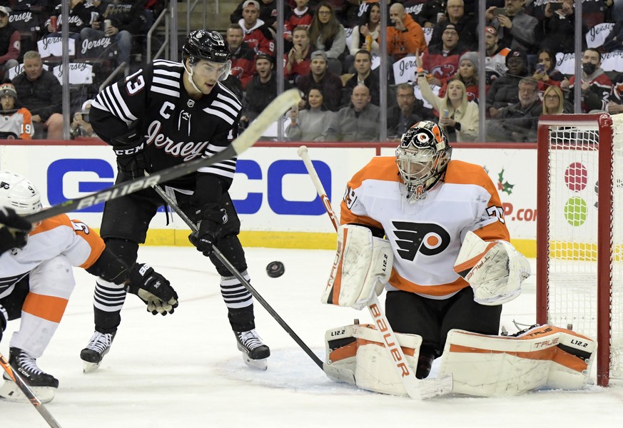 Philadelphia Flyers goaltender Carter Hart (79) deflects the puck as New Jersey Devils center Nico Hischier (13) looks for a rebound during the first period of an NHL hockey game Wednesday, Dec. 8, 20 ...