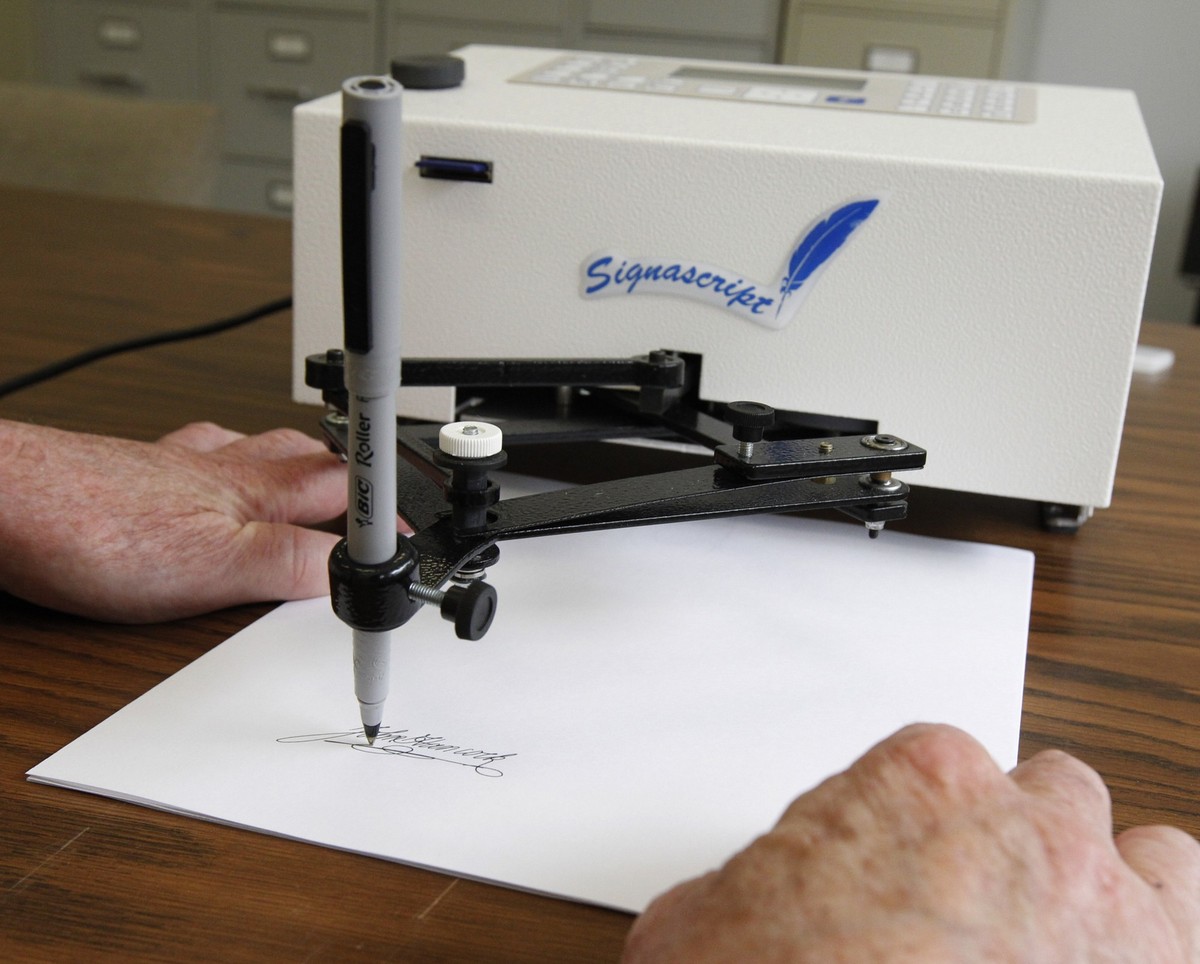 Damilic Corp. president Bob Olding anchors a sheet of paper as the Atlantic Plus, the Signascript tabletop model autopen, produces a signature at their Rockville, Md., office, June 13, 2011. (AP Photo ...